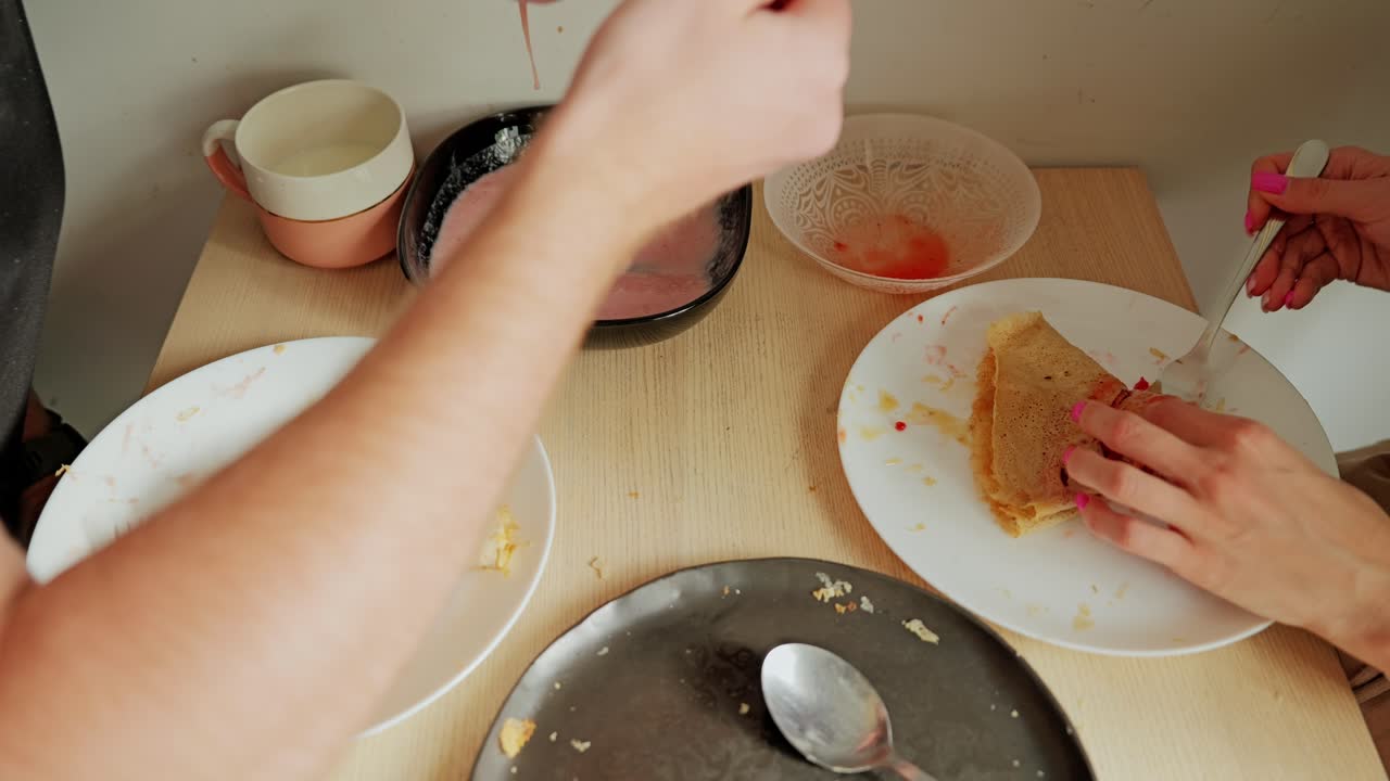 Warm, intimate breakfast moment as young couple rolls crepes with pink filling