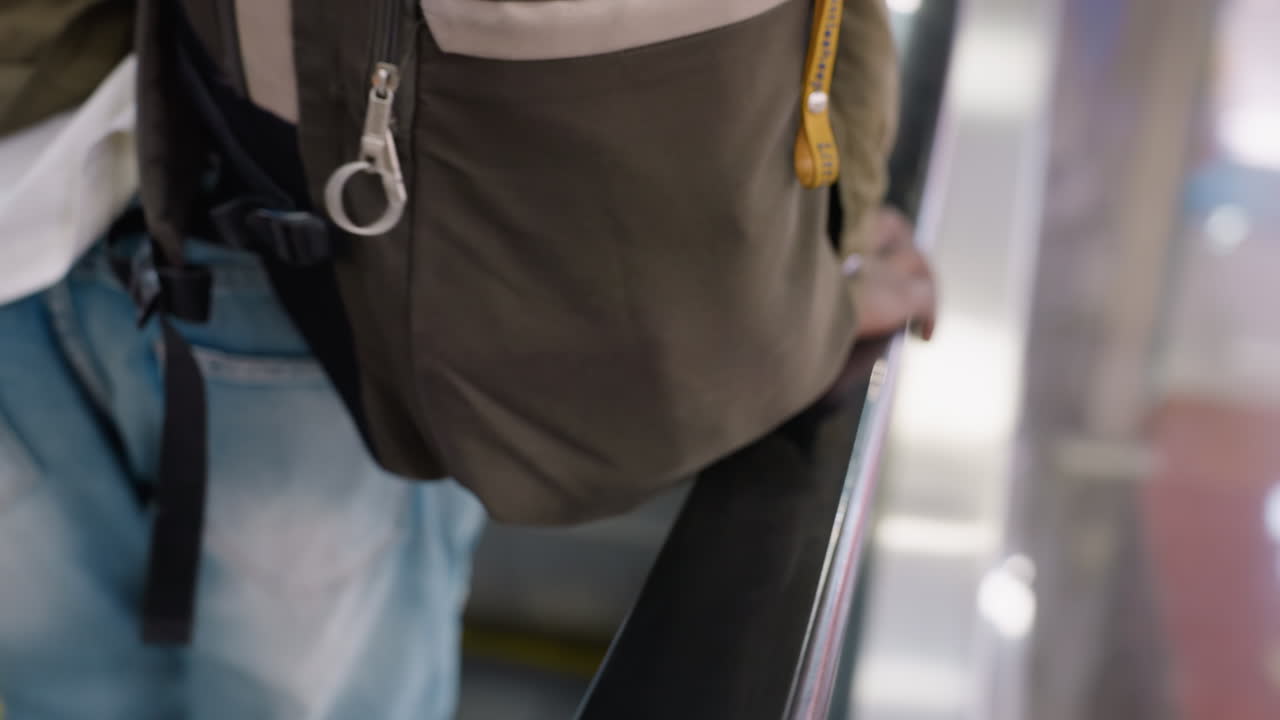 Close up rear view of person stepping onto moving escalator holding black handrail with background showing metallic stairs, yellow safety lines and blurry motion