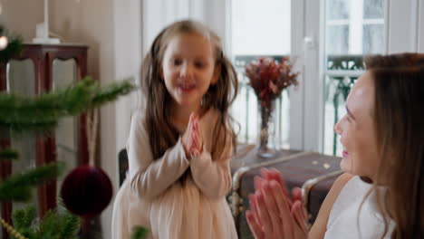 Smiling-woman-hanging-xmas-toy-at-branch-portrait.-Overjoyed-baby-clapping-hands