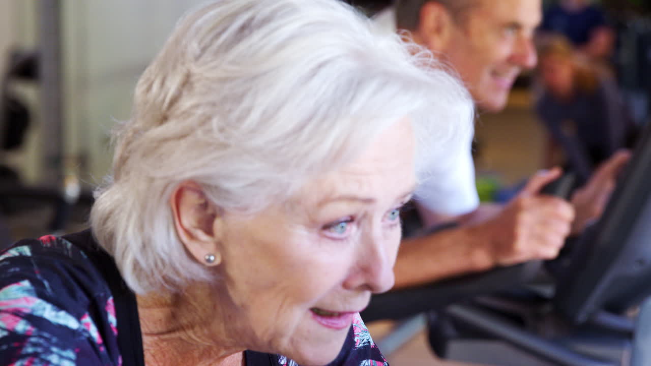 фокусный снимок активной пожилой пары, занимающейся упражнениями на велосипедных машинах в тренажерном зале.