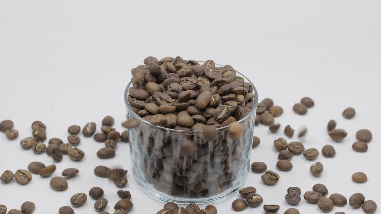 Cena em câmera lenta de grãos de café caindo em uma xícara transparente. Em um fundo branco.