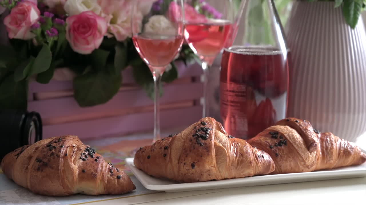 Primo piano di croissant e calici di rosé su un tavolo con un cesto rosa di fiori