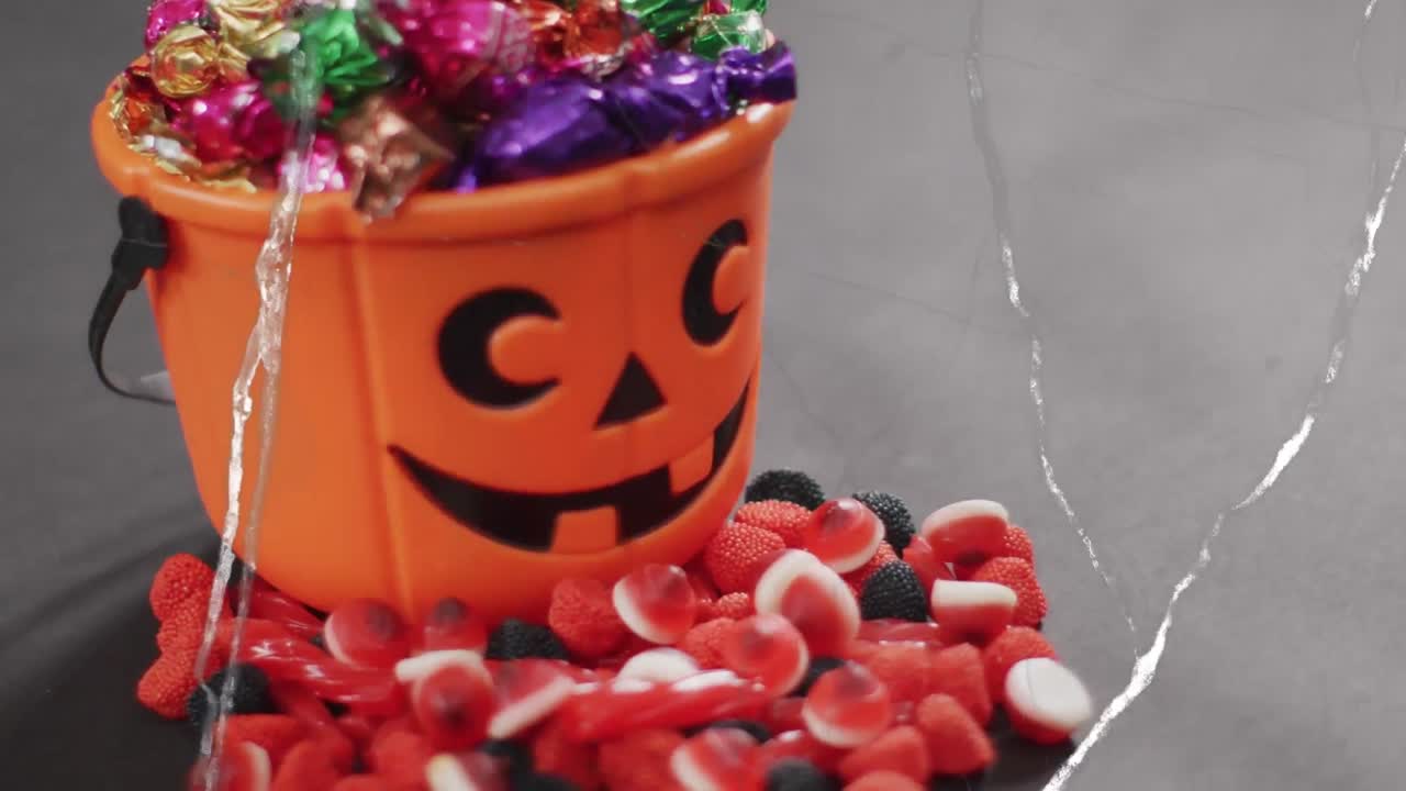 Animation of halloween carved pumpkin bucket with sweets on grey background