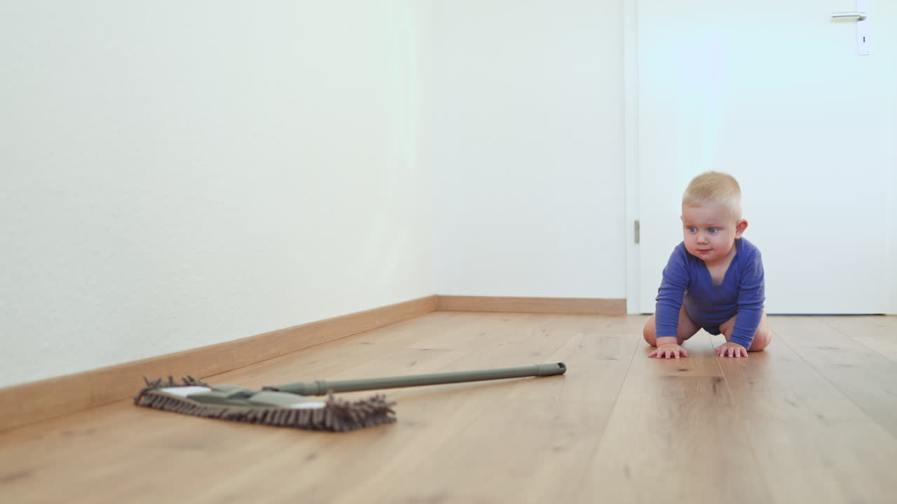 Un bambino piccolo lava il pavimento con un mop. Il bambino aiuta a pulire il pavimento. Un bambino in un body di cotone