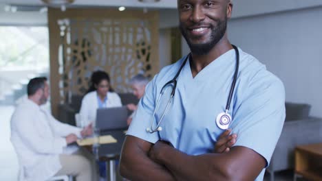 portrait of african american male doctor smiling, with colleagues in discussion in background