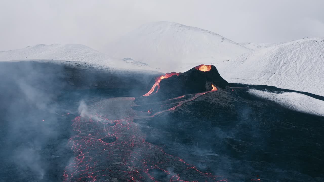 Effusive volcano with steadily flowing lava field surrounded by snowy mountains