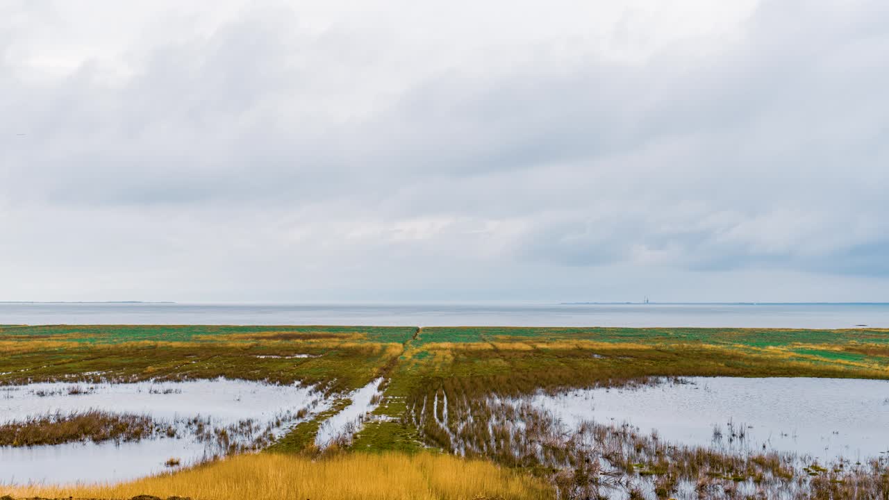 Timelapse scene of tranquil wetlands and marshes with reflections under cloudy skies near the East Frisian Islands, Lower Saxony, Germany. Rain clouds move peacefully over the wetlands.