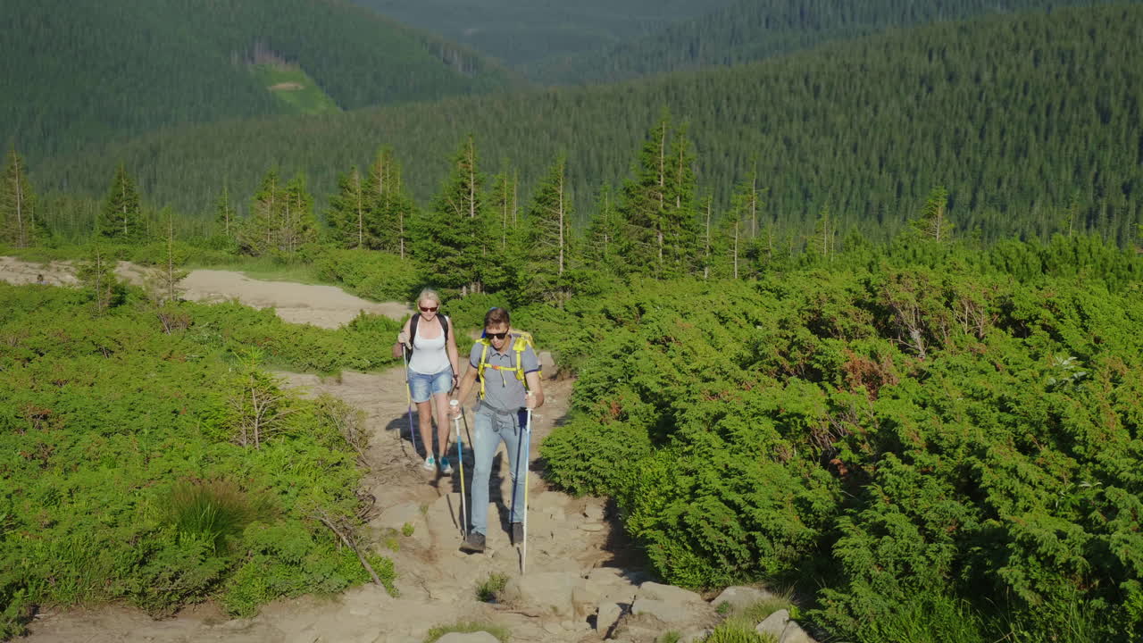 Una coppia di viaggiatori con zaini sale il sentiero di montagna Video 4K