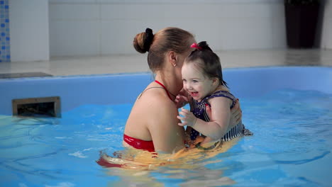 Cute-little-baby-and-his-mother-having-swimming-lesson-in-the-pool.-The-Mother-is-holding-his-son-in-his-hands-and-embracing-him.-Little-boy-is-happily-smiling