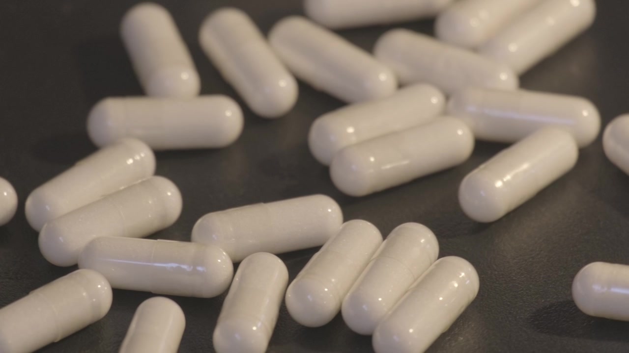 Capsule bianche che cadono e rotolano su uno sfondo nero, mostrate al rallentatore.