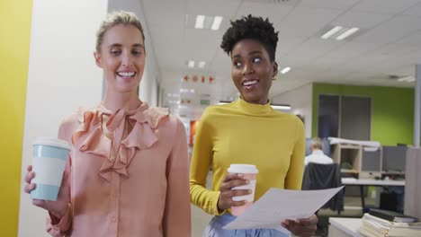 felices y diversas compañeras de trabajo hablando y caminando en la oficina.