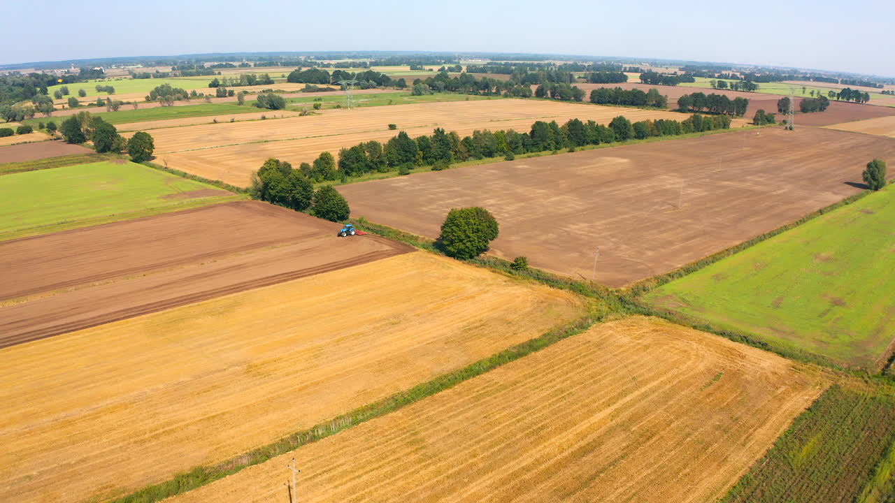 Aerial view of drone flying above farmland with tractor on the field