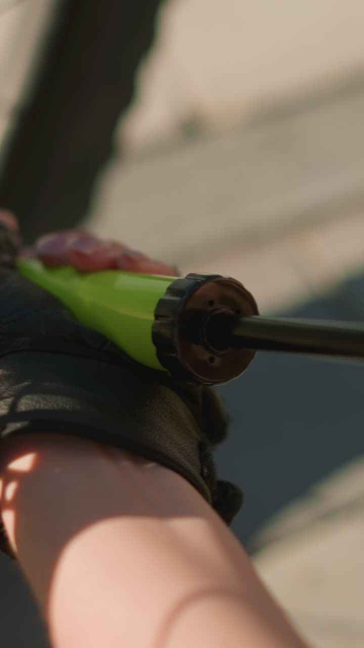 primer plano de manos con guantes bombeando aire intensamente en el neumático de la bicicleta usando una boquilla verde en un día soleado, el fondo suavemente borroso, mostrando detalles sutiles de los radios y el pavimento