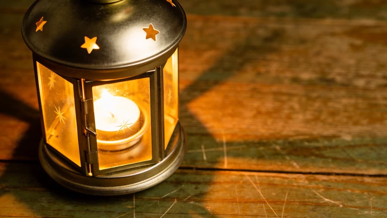Candela tealight che sfarfalla in una lanterna di metallo, rivelando un caldo bagliore su legno graffiato, con spazio per il testo.