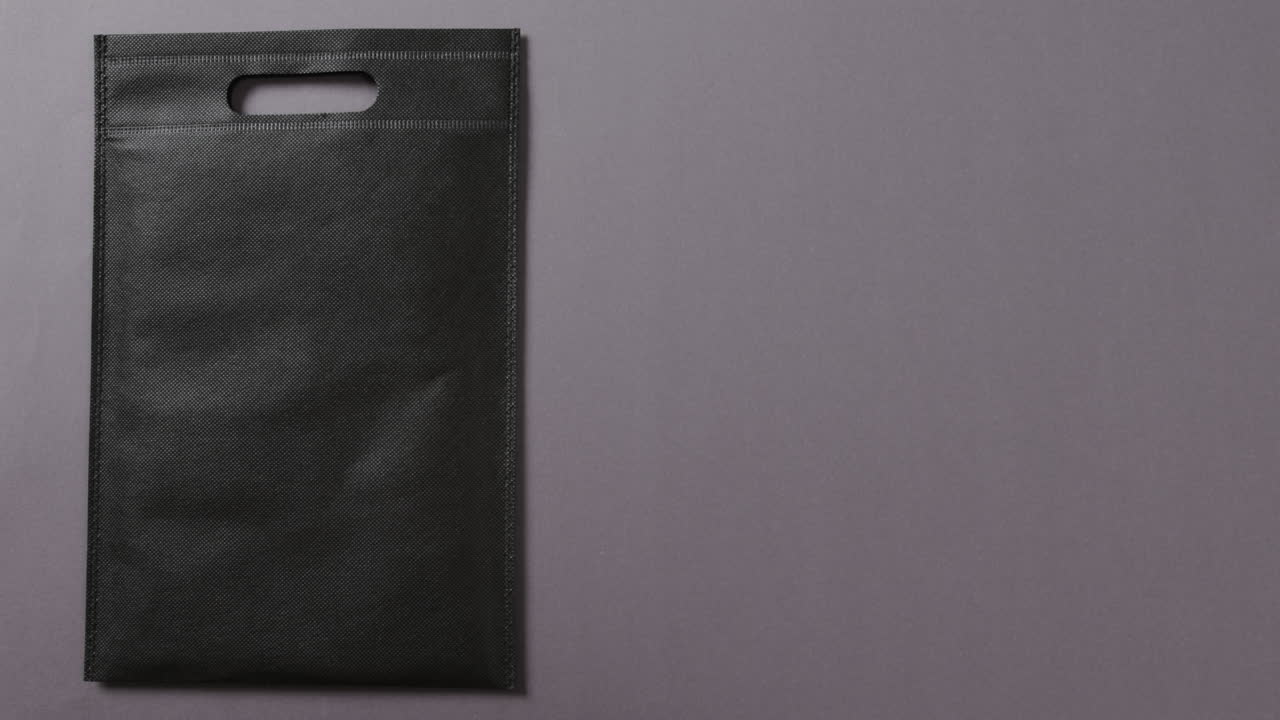 Primo piano di borsa nera su sfondo grigio, spazio per il testo, slow motion