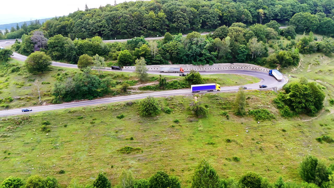Curving road through green forested hills during daytime. A winding road navigates through lush green hills, with vehicles traveling and trees lining the roadside