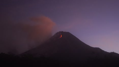 glowing lava avalaches during the eruption of the merapi volcano at the night with a purplish sky background