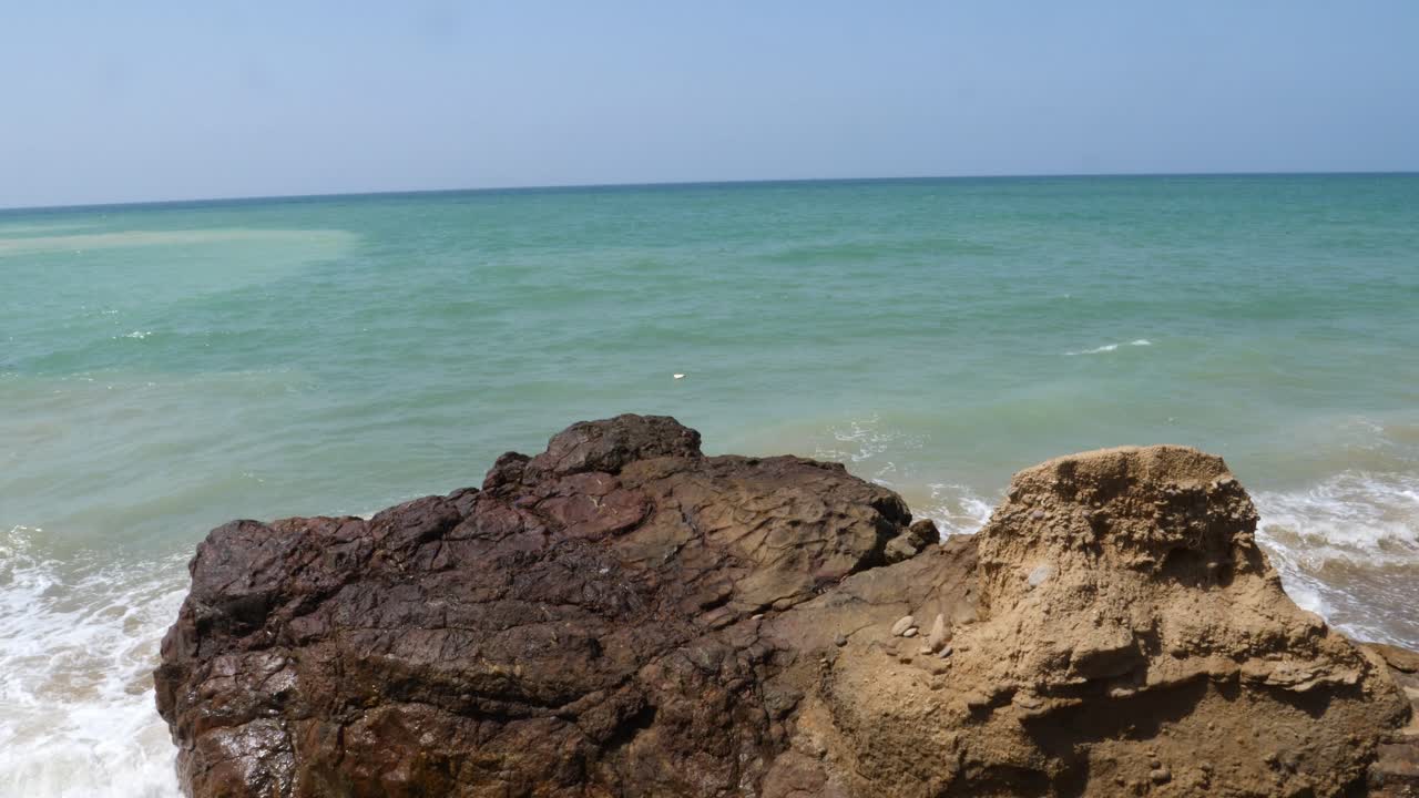 Onde oceaniche che arrivano lentamente e si infrangono sulla spiaggia, viste da una roccia.