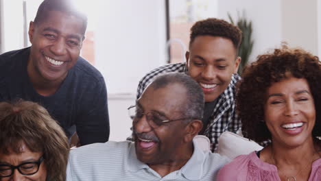 multi generation black family sit relaxing together at home smiling to camera, close up panning shot