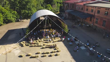 Menschen-Sitzen-Vor-Einem-Offenen-Hangar,-Sitzen-Auf-Heuballen-Und-Schauen-Sich-Ein-Konzert-An