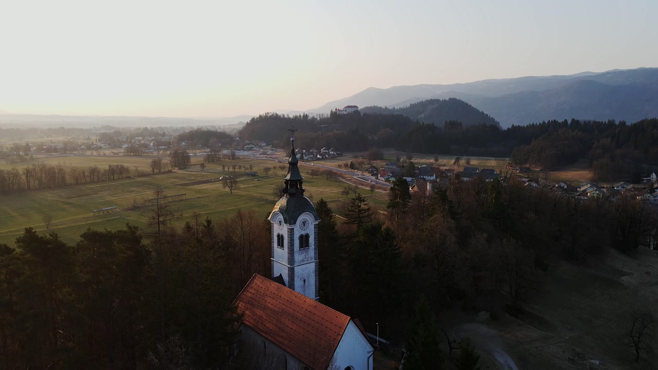 Cinematic aerial view of St Andrew Church in Bled Slovenia glowing sunrise