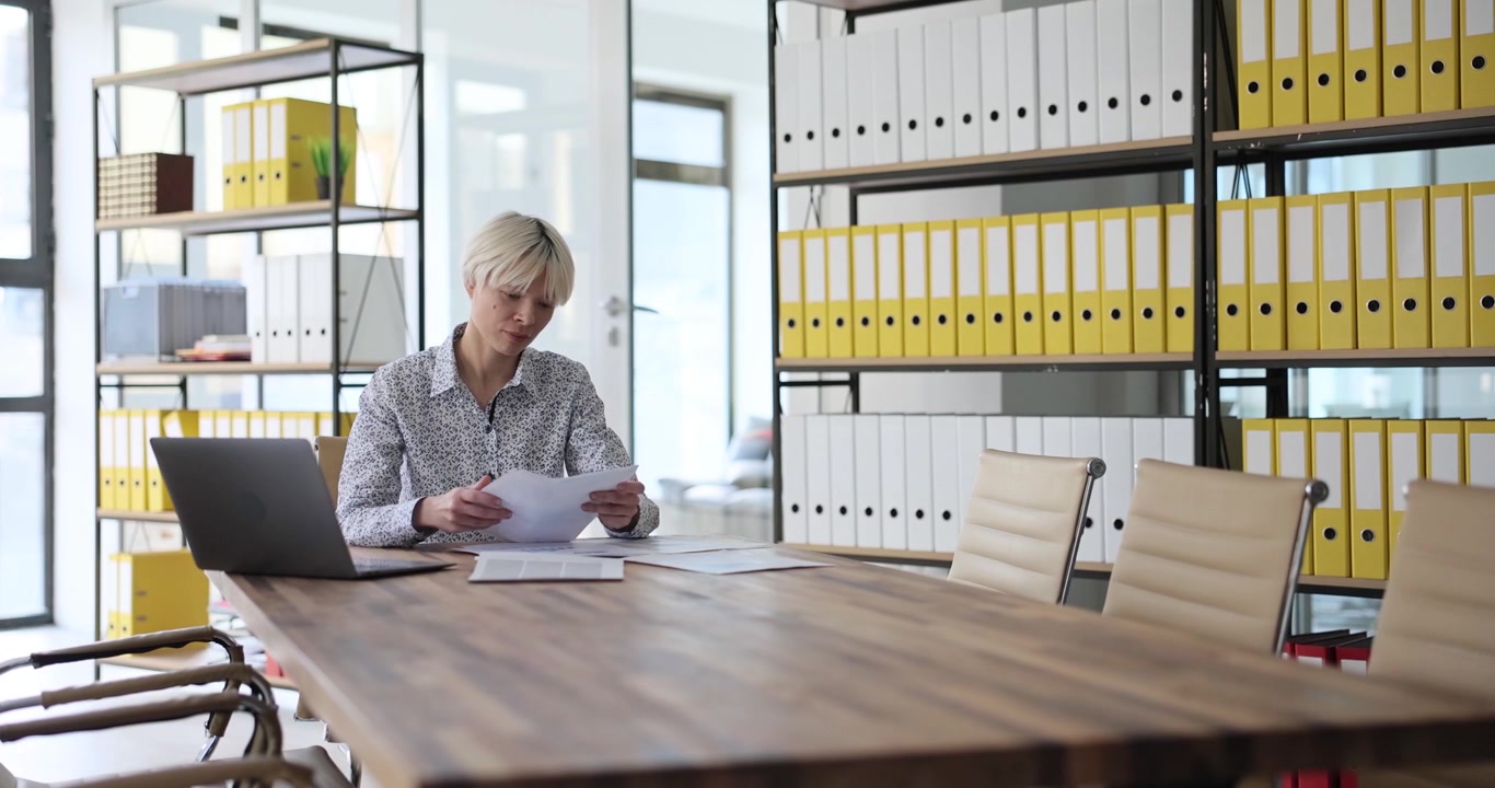 Woman sitting at long conference table reviews documents