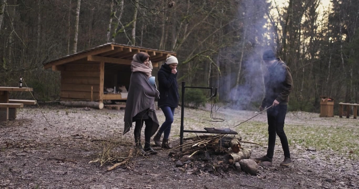 Campingvenner står omkring lejrbålet, mens de laver mad.