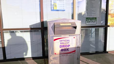 man votes by dropping mail-in ballot letter in slot at voting booth with offical ballot drop box sign for democratic government election in presidential race