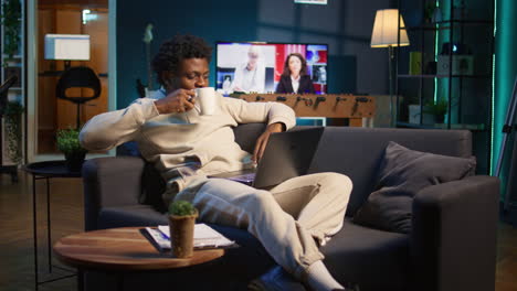 positive african american man multitasking on a laptop in stylish loft, fully connected to the internet while managing his freelance work and remote responsibilities. browsing web at home. camera b.