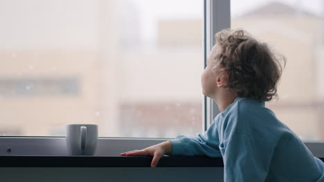 un lindo bebé está sentado cerca de la ventana de su casa viendo caer la nieve en la calle durante la navidad y el milagro