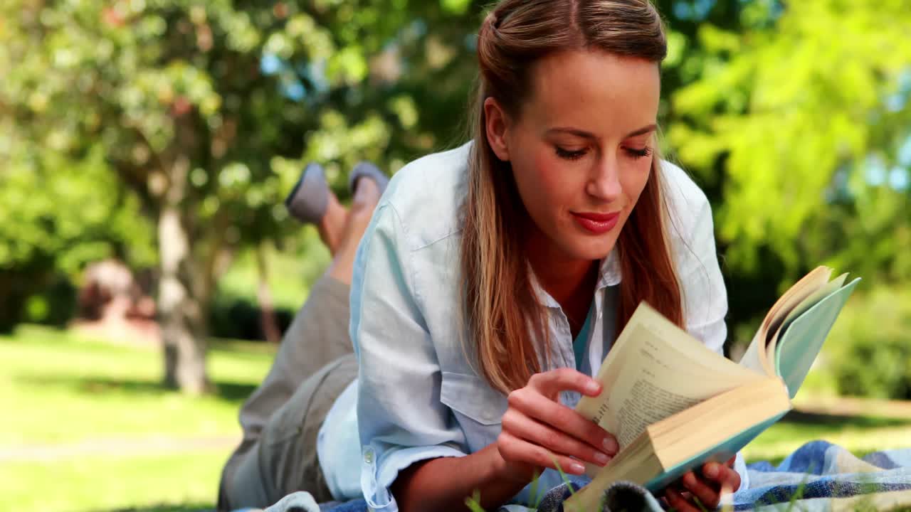 bonita rubia leyendo un libro acostada en una manta en el parque