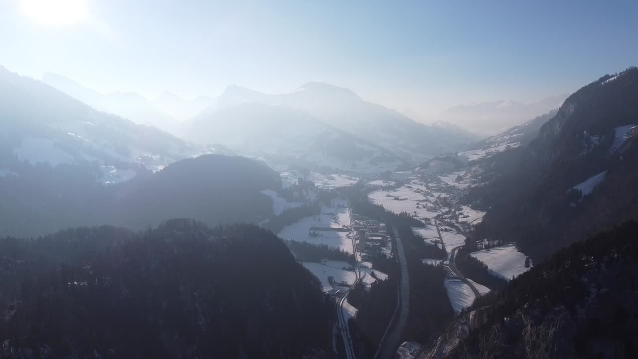 Drone flight through a foggy and snow-covered valley with lots of forest in the Swiss mountains