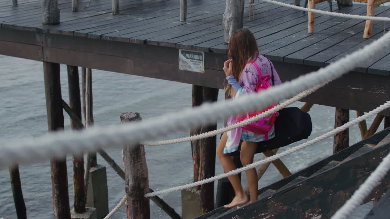Young woman with snorkeling equipment bag goes down a wooden pier to embark a tour boat