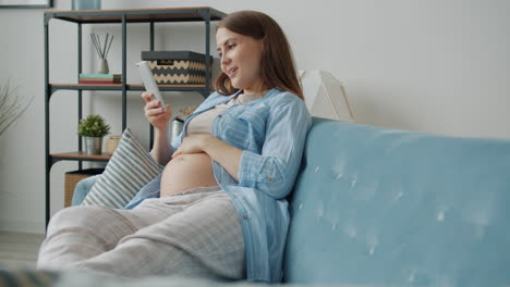 pregnant woman relaxing on couch with smartphone