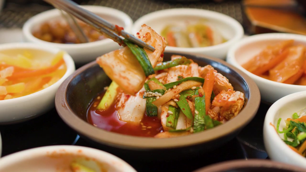 Sumpit logam mengambil kimchi kubis pedas dari berbagai lauk pauk tradisional Korea