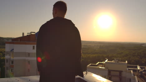 a man with a laptop walks on the roof at sunset and looks at the city from a height at sunset.