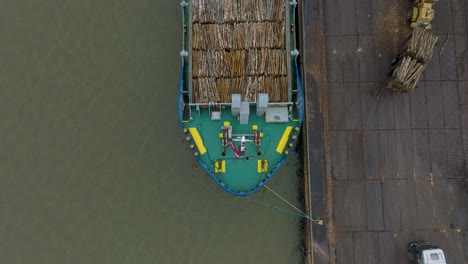 aerial birdseye view of wood terminal crane loading timber into the cargo ship, port of liepaja , lumber log export, overcast day with fog and mist, wide drone shot moving backward, tilt up