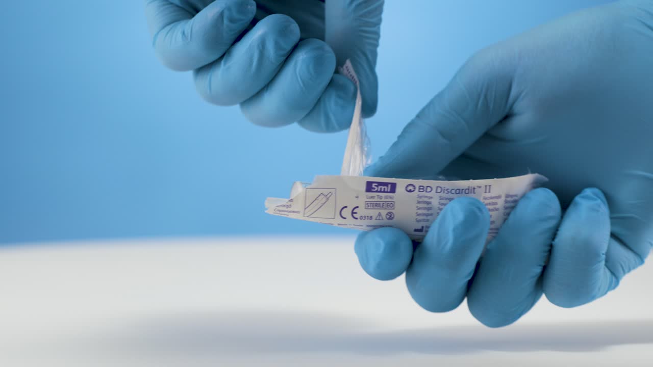 preparación para la cirugía, el médico jefe abre el paquete de jeringa estéril, fondo azul