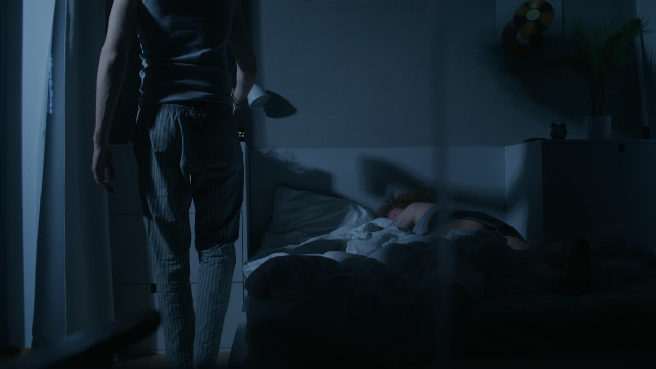 夜寝ているパートナーを見ながらベッドのそばに座っている男性