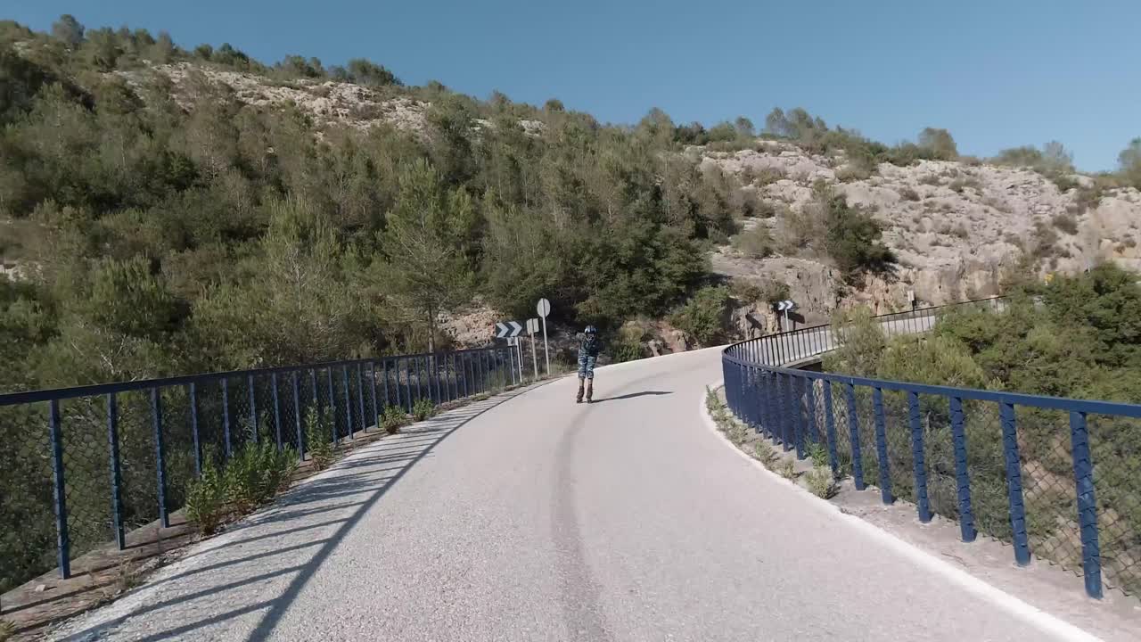 Front facing follow shot of roller skater crossing a bridge in a mountain road