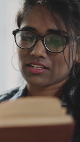 indian woman in glasses flips pages of textbook looking for information to work on educational report. student reads book on blurred background closeup