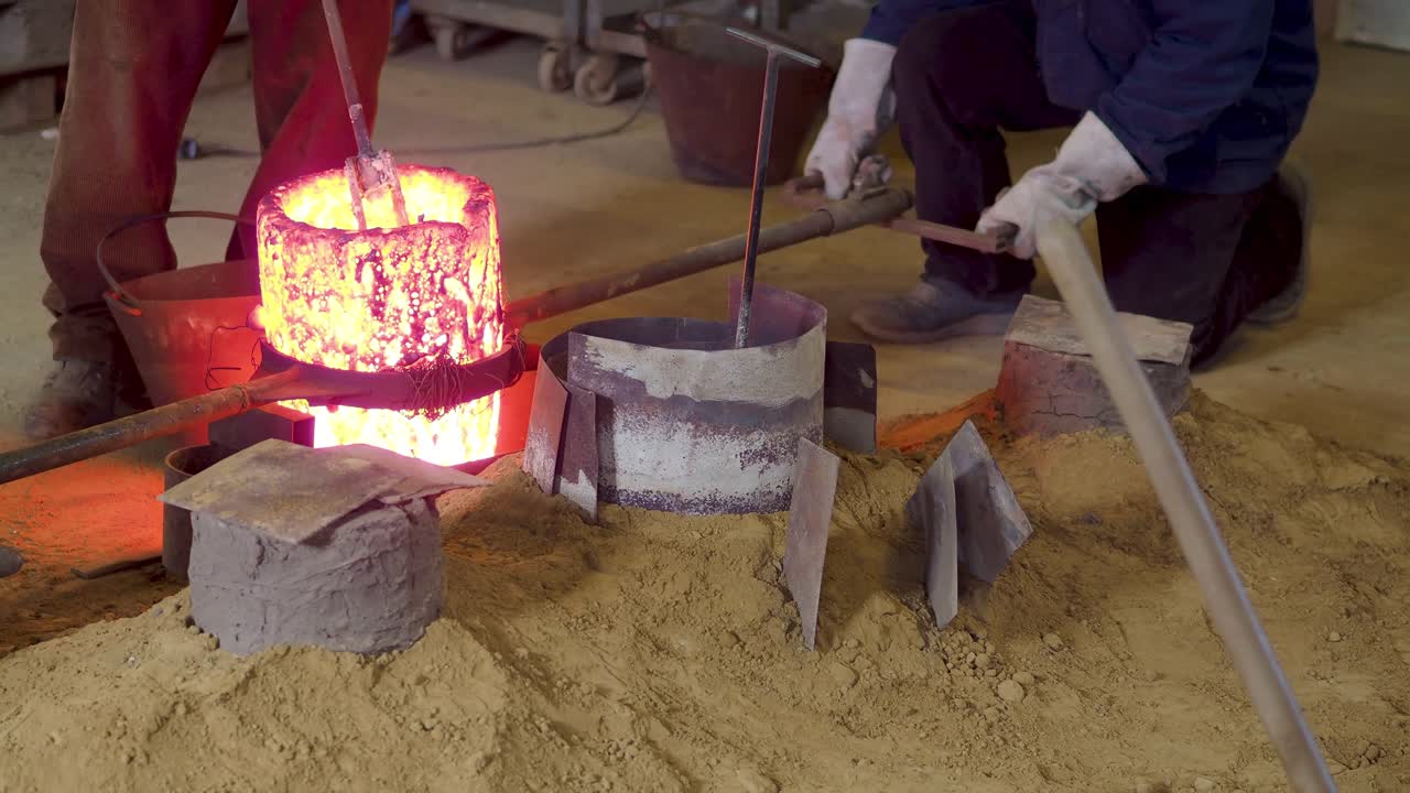 Ancient floor crucible glows with molten metal as artisans kneel to transfer the alloy using rods in a bell casting foundry, fine sand insulation surrounds the setup, slow motion