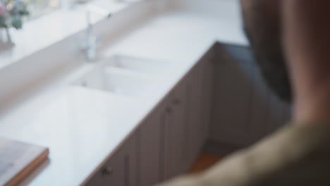 close up of male american soldier in uniform looking at cap badge in kitchen on home leave