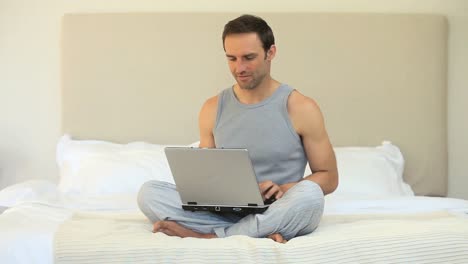 Man working on a laptop sitting on the bed