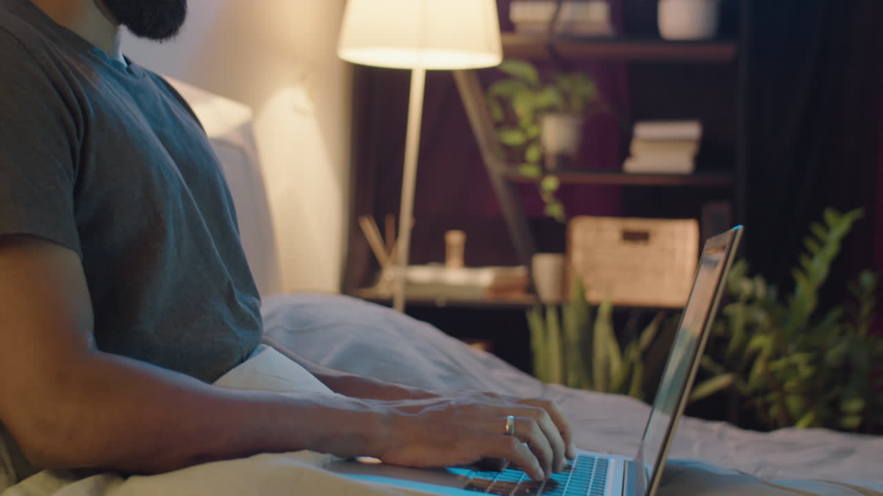 Man Using Laptop on Bed in Evening at Home