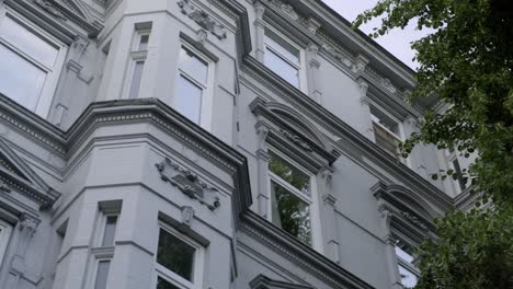 grey facade of a beautiful european residential building in victorian style from low angle, with green tree foliage growing at the wall