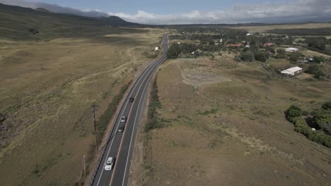 Highway-past-village-in-green-rolling-volcanic-hills-landscape,-Hawaii