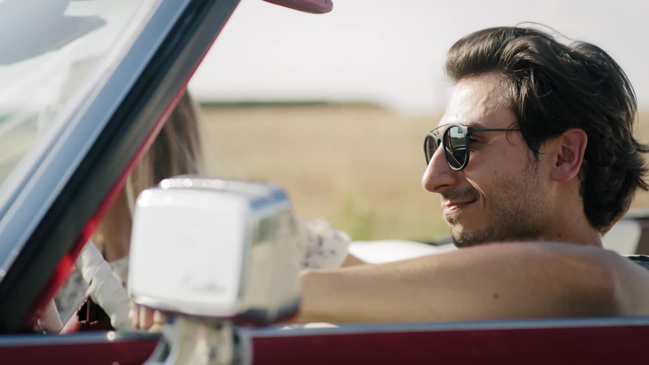 vista lateral de una pareja conduciendo en un cabriolet rojo