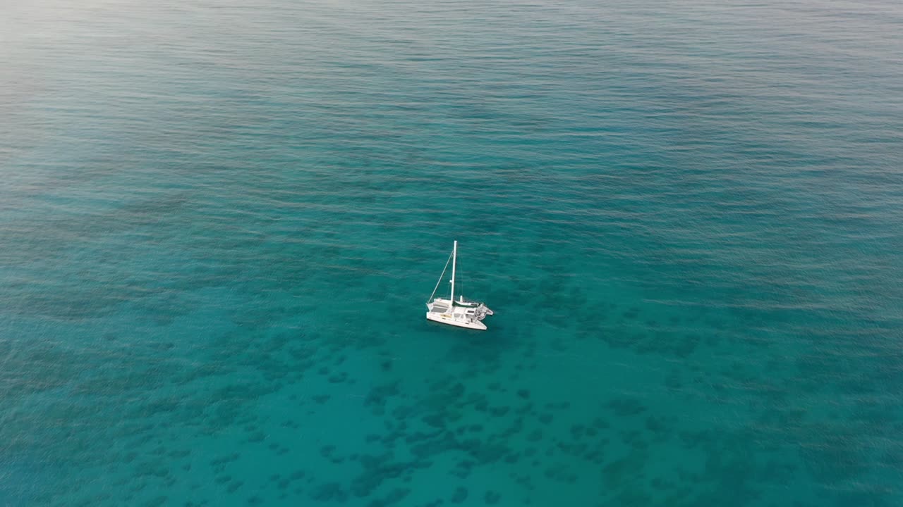 la órbita aérea del catamarán flotando pacíficamente en aguas tranquilas y claras del océano, el mar tranquilo y el aislamiento del barco crean una escena marina pacífica y pintoresca