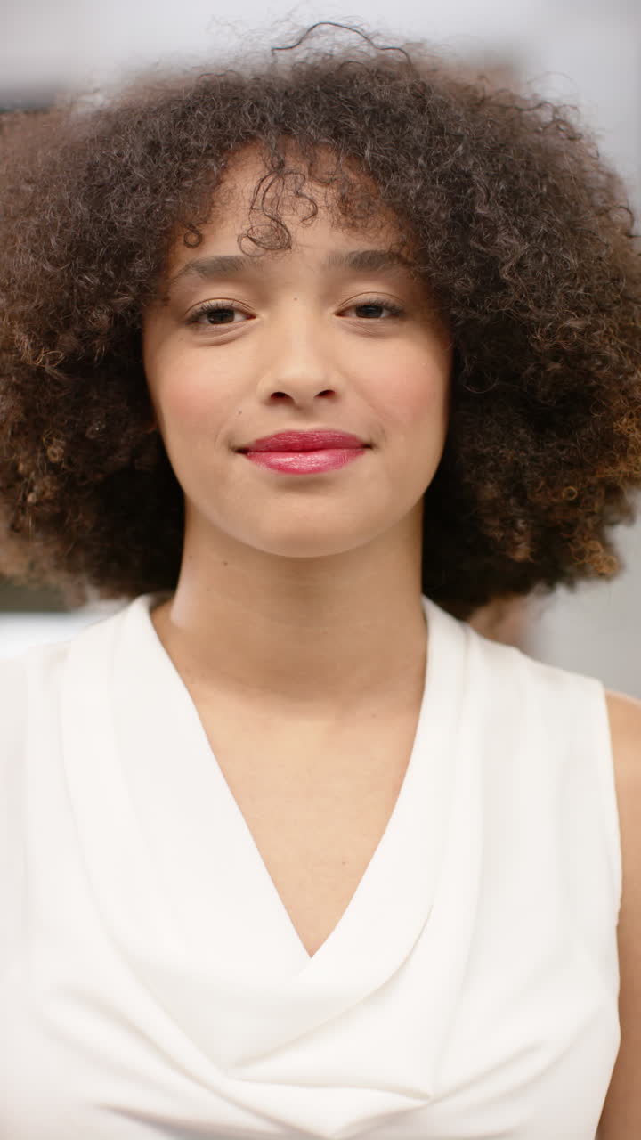 Vertical video of portrait of happy biracial businesswoman in office in slow motion
